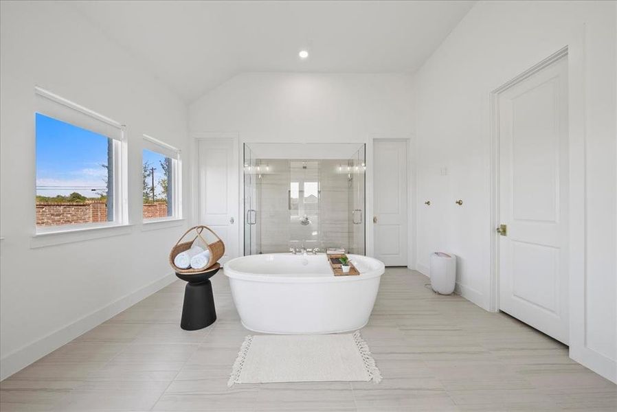 Full bathroom featuring lofted ceiling, a freestanding tub, a shower stall, and baseboards