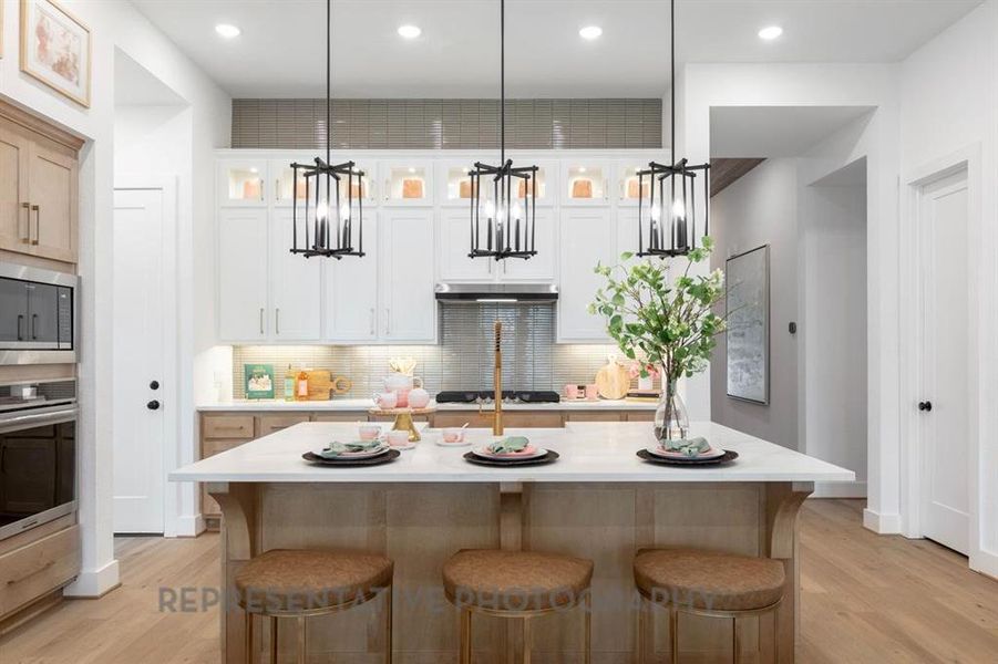 Kitchen with a kitchen bar, decorative light fixtures, glass insert cabinets, appliances with stainless steel finishes, and white cabinets