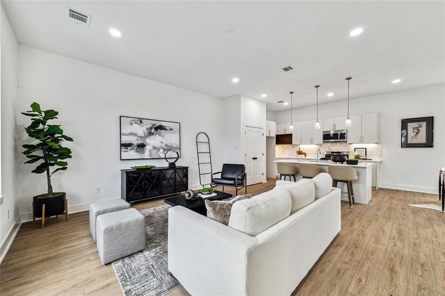 Inviting open-concept living area featuring sleek hardwood floors, modern lighting, and a seamless flow into the stylish kitchen, perfect for relaxation and entertaining.