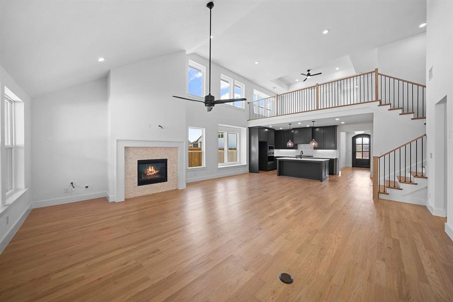 Unfurnished living room with a glass covered fireplace, a ceiling fan, high vaulted ceiling, recessed lighting, and light wood-style floors Unfurnished living room with a glass covered fireplace, a ceiling fan, high vaulted ceiling, recessed lighting, and light wood-style floors