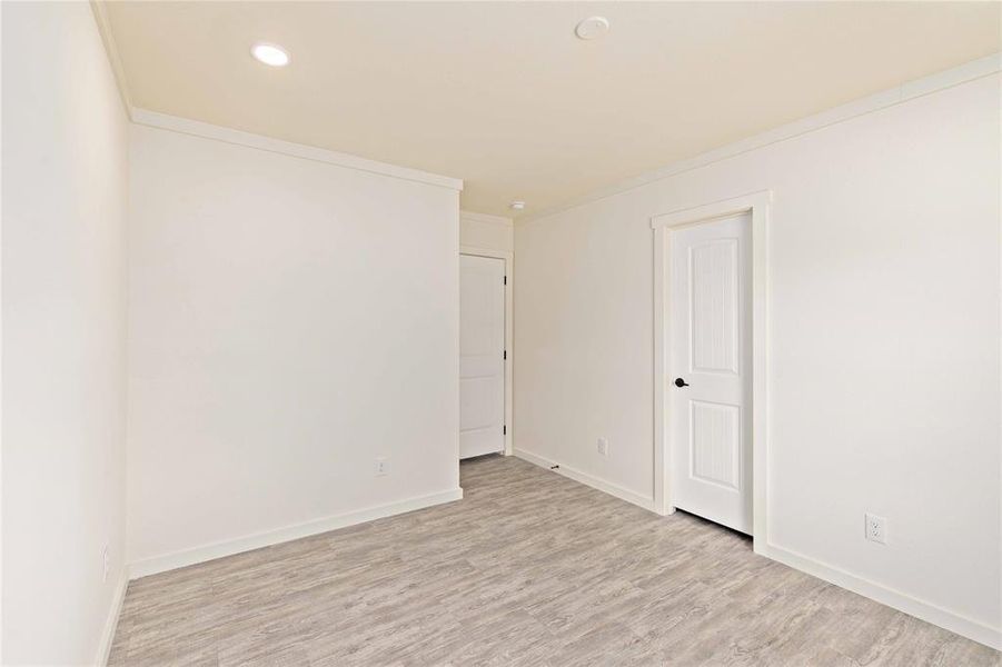 Room featuring wood-finish flooring, recessed ceiling lighting, two white paneled doors with black hardware, and white trim
