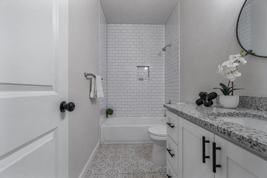 Full bathroom with vanity, tile patterned floors, tiled shower / bath, and toilet