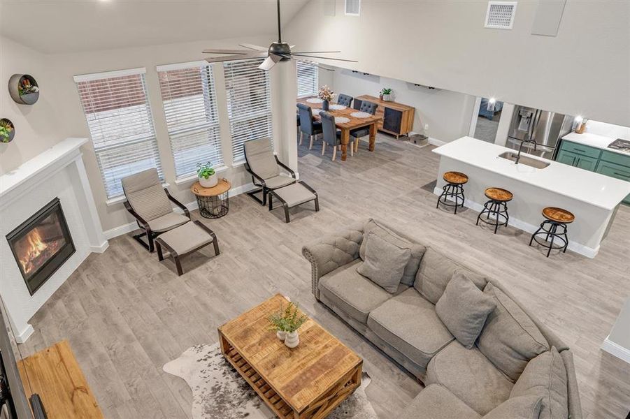 Living room featuring ceiling fan, a glass covered fireplace, light wood-style floors, and lofted ceiling