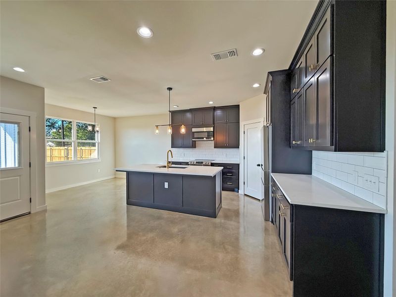 Kitchen featuring decorative backsplash, finished polished concrete floors, pendant lighting, recessed lighting, and a kitchen island with sink