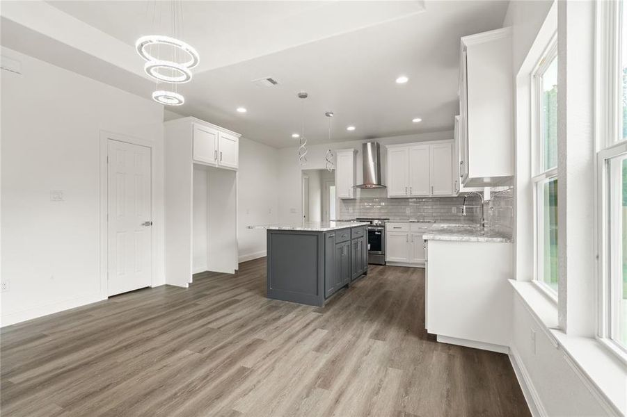 Contemporary kitchen featuring a gray island, white cabinetry, a subway tile backsplash, stainless steel range hood, and wood-finish flooring
