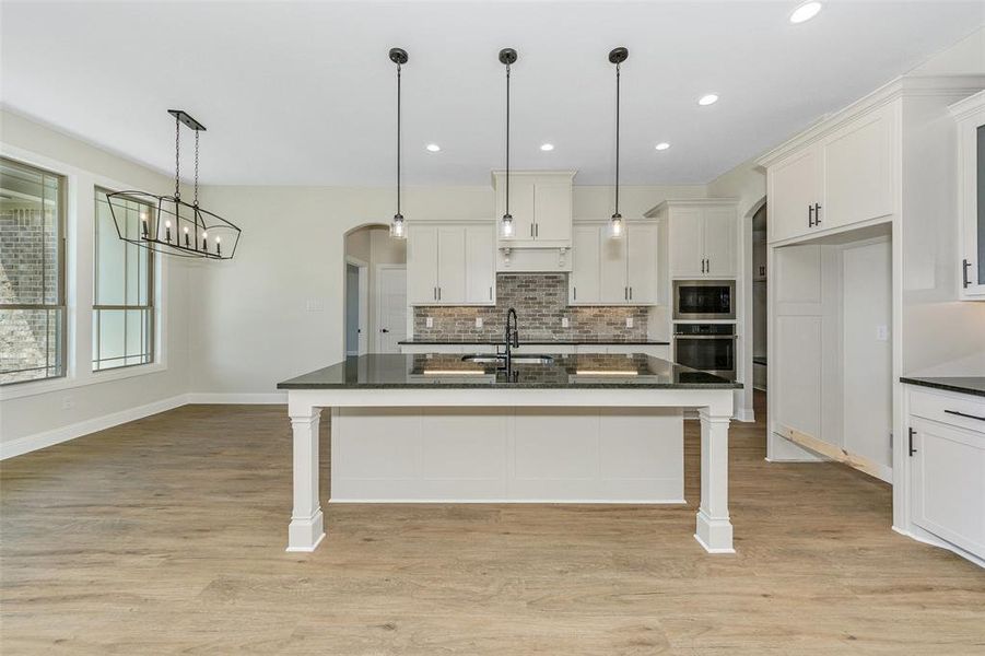 Kitchen with a kitchen breakfast bar, light hardwood / wood-style flooring, appliances with stainless steel finishes, a kitchen island with sink, and white cabinets