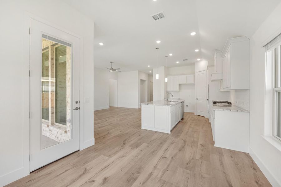 Open kitchen and living area with white cabinets, center island, light wood floors, and glass back door Open kitchen and living area with white cabinets, center island, light wood floors, and glass back door