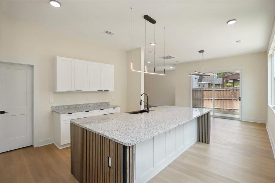 Kitchen featuring pendant lighting, white cabinets, a kitchen island with sink, and sink