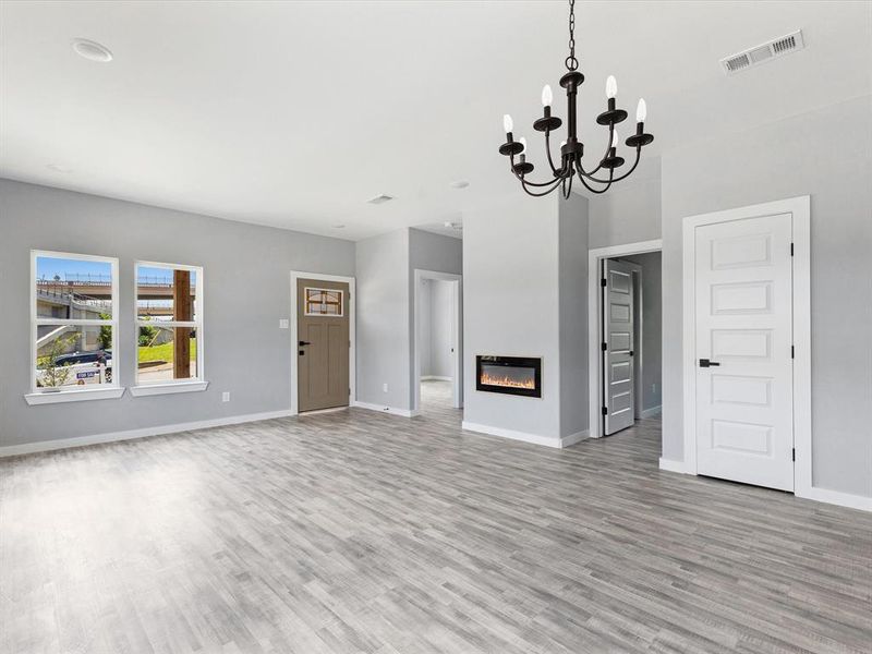 Unfurnished living room with light wood-style floors, baseboards, a chandelier, and a glass covered fireplace