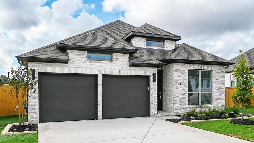 French country inspired facade with roof with shingles, driveway, an attached garage, and brick siding