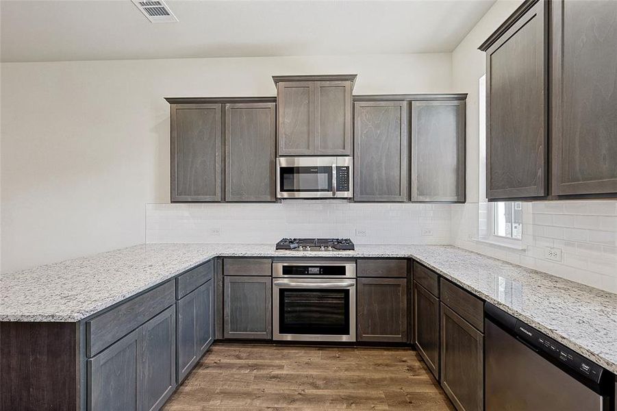 Kitchen featuring light stone counters, appliances with stainless steel finishes, decorative backsplash, and dark brown cabinetry