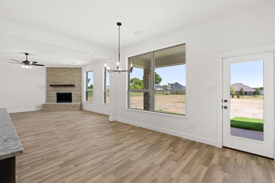 Unfurnished living room with a fireplace, a chandelier, light wood finished floors, and ceiling fan Unfurnished living room with a fireplace, a chandelier, light wood finished floors, and ceiling fan