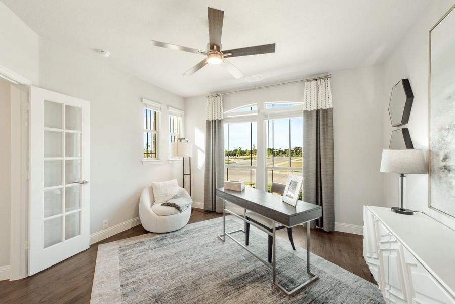 Home office with dark wood desk, ceiling fan, hardwood floors, and large windows with gray curtains