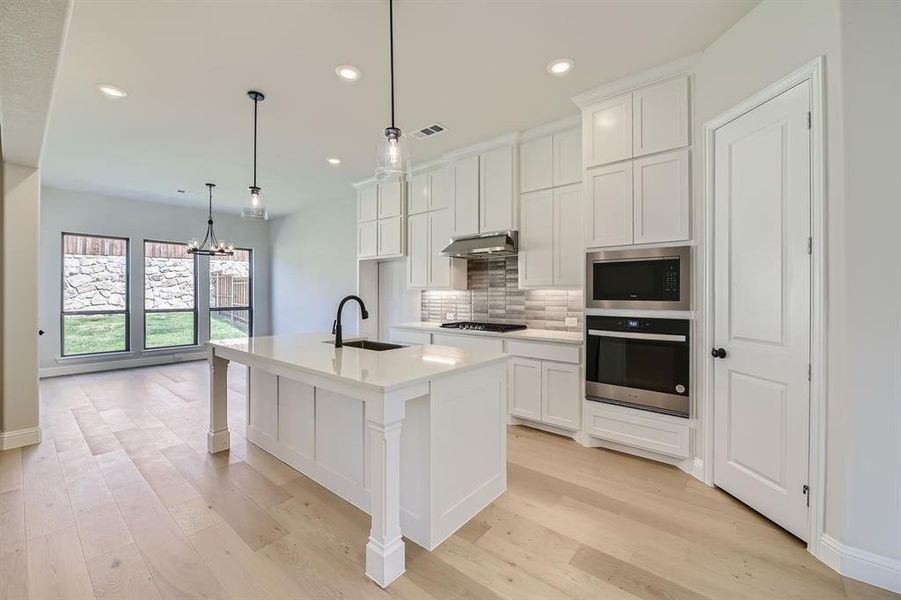 Kitchen with light hardwood / wood-style floors, appliances with stainless steel finishes, sink, decorative backsplash, and a center island with sink