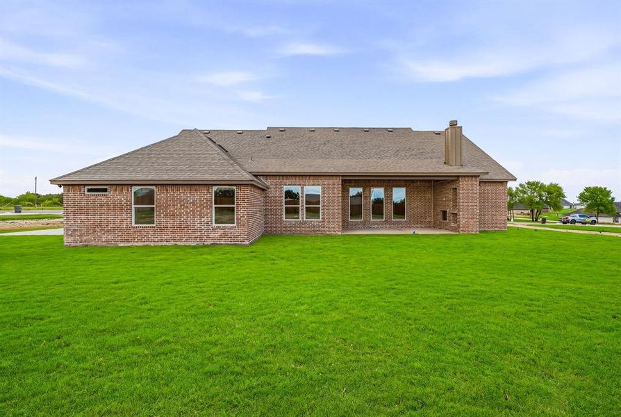 Back of property with brick siding, roof with shingles, a chimney, a patio, and a yard