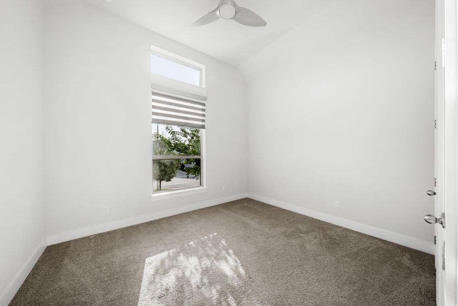 A well-lit bedroom features plush carpeting and a large window overlooking lush greenery.