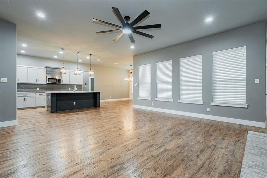 Unfurnished living room featuring recessed lighting, light wood finished floors, ceiling fan with notable chandelier, and baseboards Unfurnished living room featuring recessed lighting, light wood finished floors, ceiling fan with notable chandelier, and baseboards
