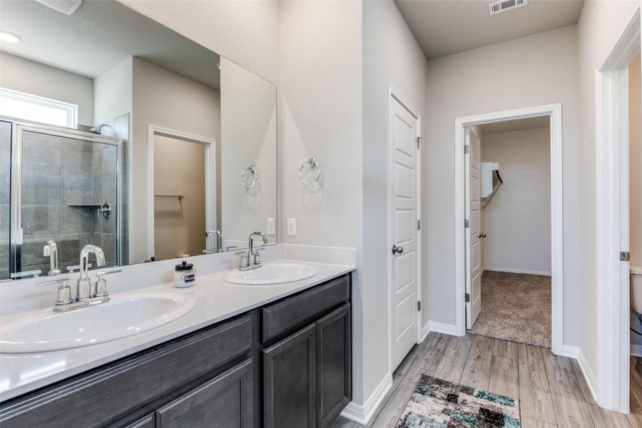 Full bath with a stall shower, double vanity, light wood-style flooring, and a spacious closet