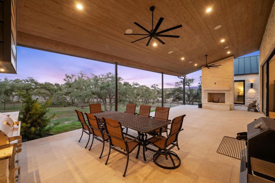 View of patio featuring an outdoor stone fireplace, outdoor dining space, grilling area, and a ceiling fan View of patio featuring an outdoor stone fireplace, outdoor dining space, grilling area, and a ceiling fan