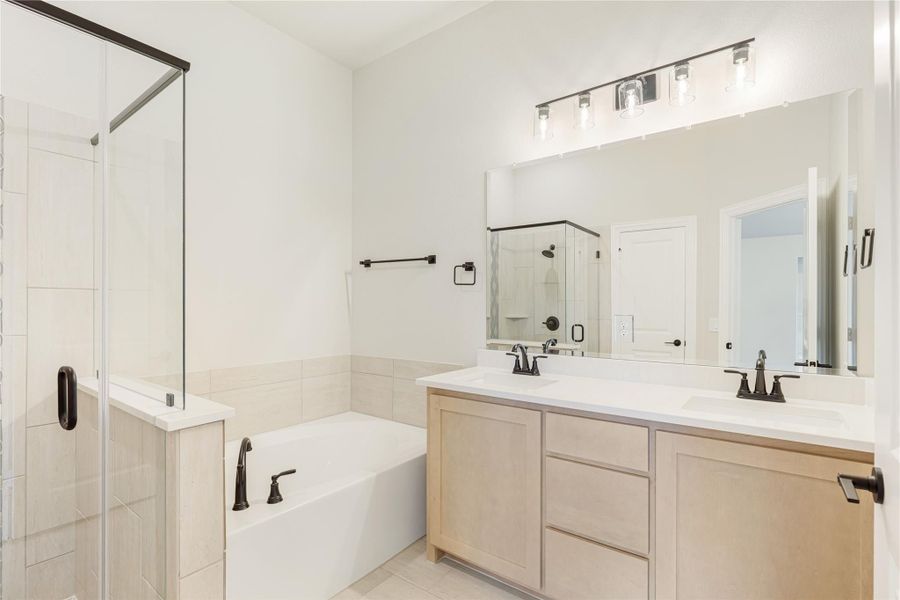 Bathroom with double sink vanity, soaking tub, and glass walk-in shower with light wood cabinets