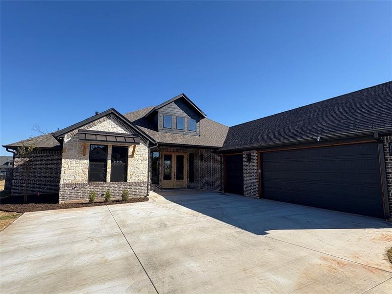 View of front of house featuring french doors, a shingled roof, concrete driveway, stone siding, and an attached garage
