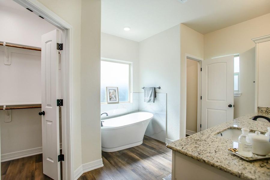 Full bath with vanity, a freestanding tub, a walk in closet, and wood finished floors Full bath with vanity, a freestanding tub, a walk in closet, and wood finished floors