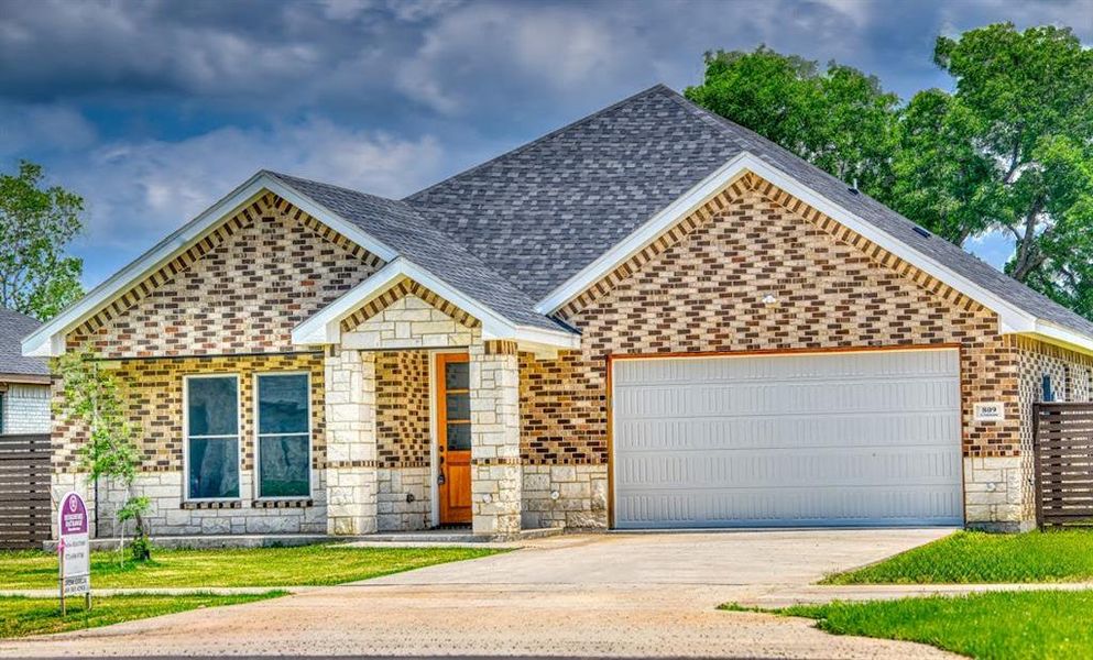 Single story home with stone siding, roof with shingles, brick siding, an attached garage, and concrete driveway Single story home with stone siding, roof with shingles, brick siding, an attached garage, and concrete driveway