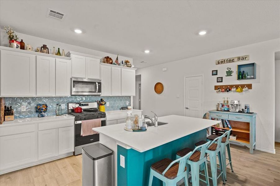 Kitchen with backsplash, stainless steel appliances, a kitchen island with sink, light hardwood / wood-style floors, and white cabinetry