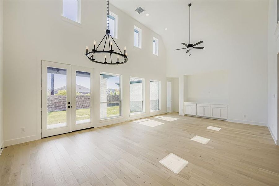 Unfurnished living room with light wood-style floors, a chandelier, a ceiling fan, a towering ceiling, and french doors Unfurnished living room with light wood-style floors, a chandelier, a ceiling fan, a towering ceiling, and french doors