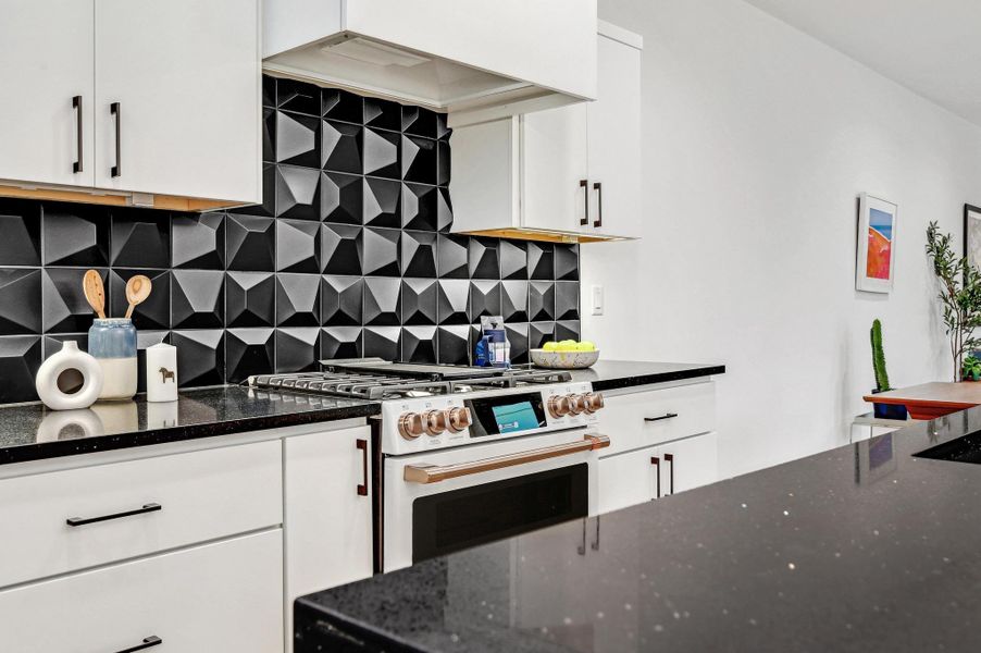 Kitchen with tasteful backsplash, dark stone countertops, high end stove, and white cabinetry