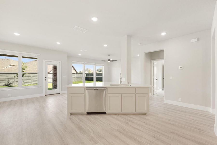Open-concept kitchen with center island, stainless dishwasher, white cabinets, and light wood floors