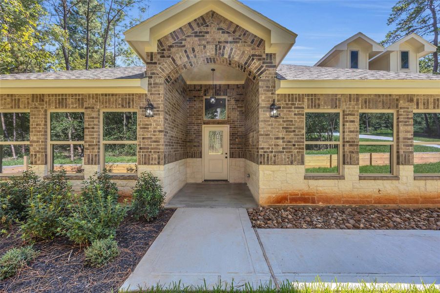 This sample of home showcases a modern brick home with a welcoming front entrance, featuring a covered porch and large windows. The house has a landscaped garden and set in a wooded area, offering a serene and private setting.