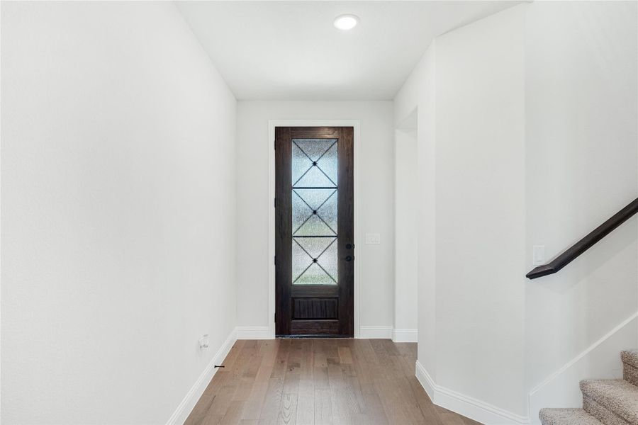 Entryway with dark wood front door featuring glass panels, hardwood floors, and staircase with carpet steps.
