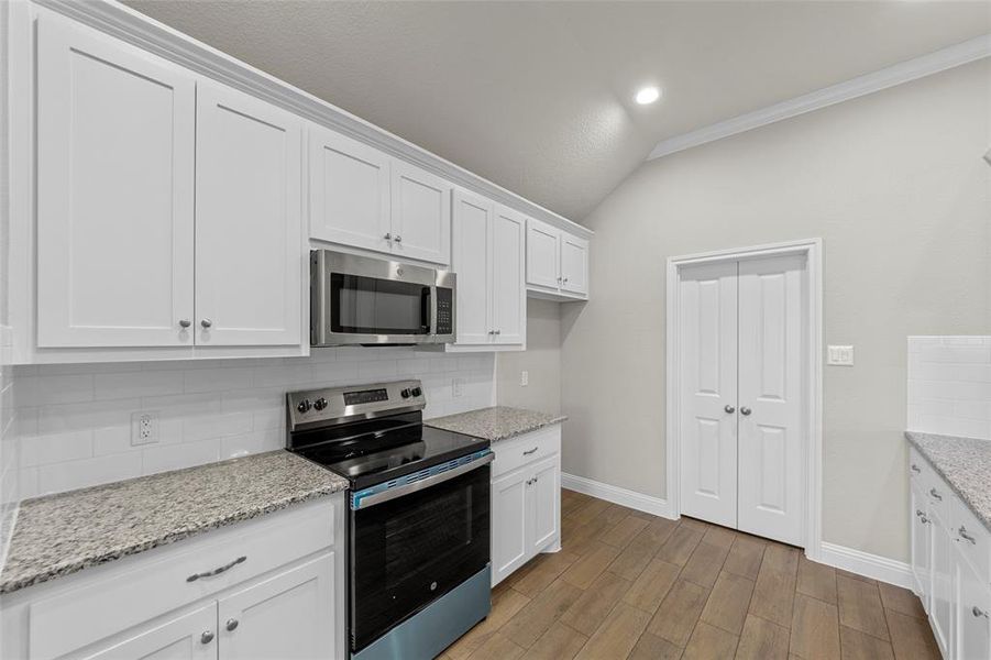 Kitchen featuring white shaker cabinetry, stainless steel appliances, speckled stone countertops, and a subway tile backsplash