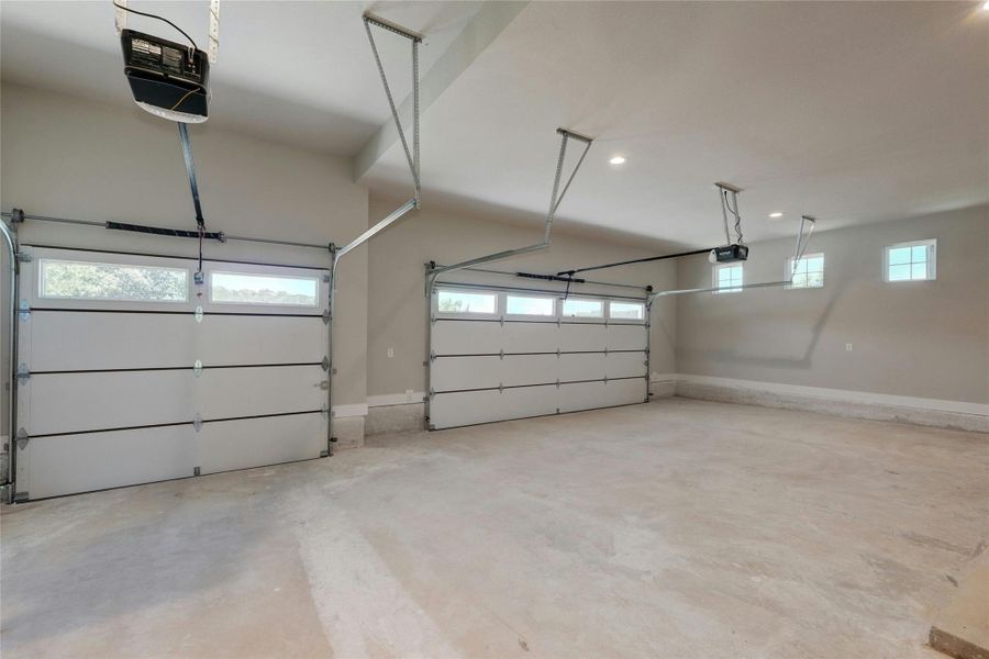 Spacious two-car garage featuring white panel doors with upper window inserts, automatic openers, and recessed lighting