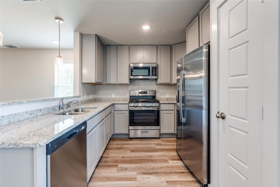 Kitchen featuring gray cabinetry, stainless steel appliances, light stone counters, and decorative light fixtures Kitchen featuring gray cabinetry, stainless steel appliances, light stone counters, and decorative light fixtures