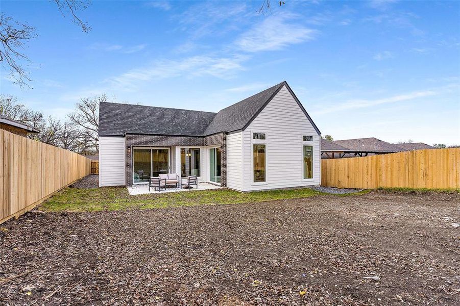 Rear view of property featuring a fenced backyard, roof with shingles, a patio, and brick siding