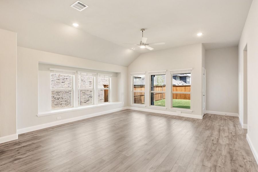 Open living room with vaulted ceiling, ceiling fan, hardwood floors, and large windows overlooking backyard