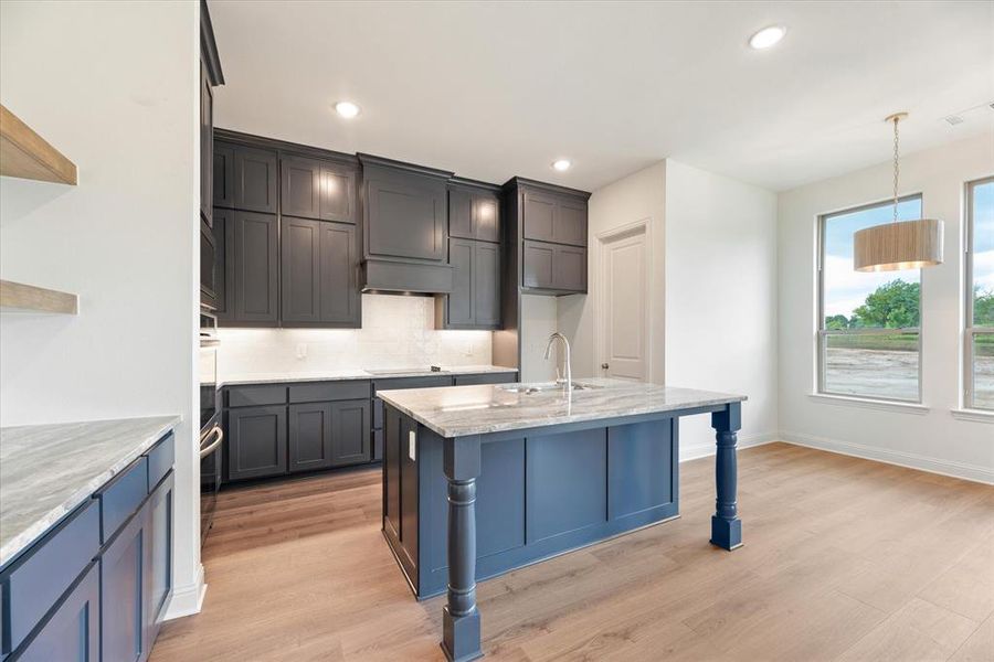 Kitchen with light hardwood / wood-style flooring, light stone counters, sink, decorative backsplash, and hanging light fixtures