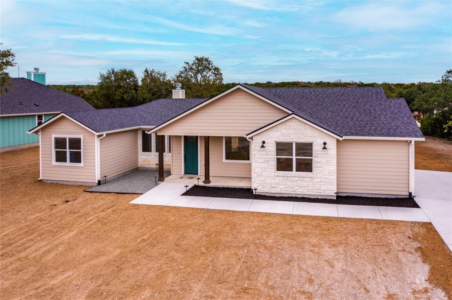 View of front of home with roof with shingles, covered porch, stone siding, and a chimney