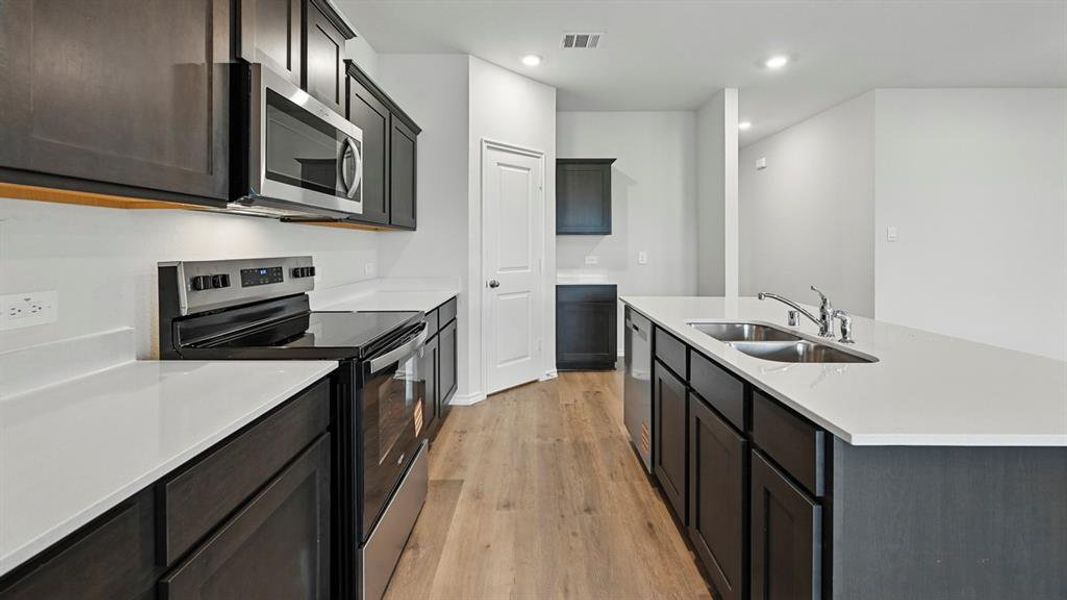 Kitchen with appliances with stainless steel finishes, an island with sink, light wood-style flooring, light stone counters, and recessed lighting