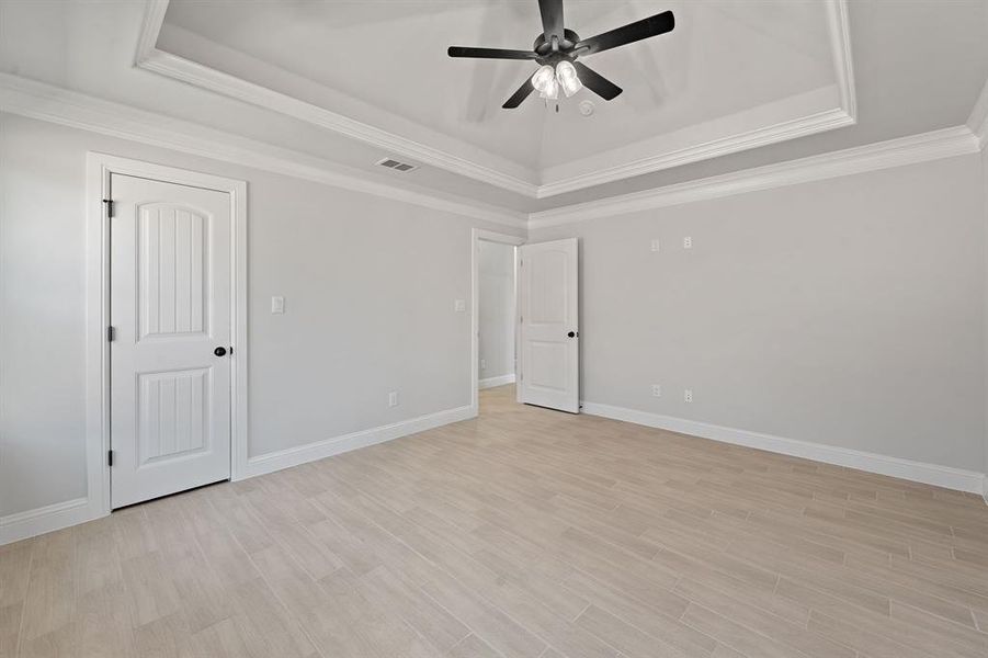Unfurnished bedroom with a raised ceiling, light wood finished floors, crown molding, and a ceiling fan Unfurnished bedroom with a raised ceiling, light wood finished floors, crown molding, and a ceiling fan