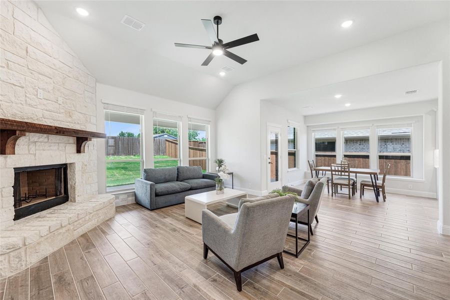 Open living and dining area with stone fireplace, vaulted ceiling, ceiling fan, and wood-look tile floors Open living and dining area with stone fireplace, vaulted ceiling, ceiling fan, and wood-look tile floors