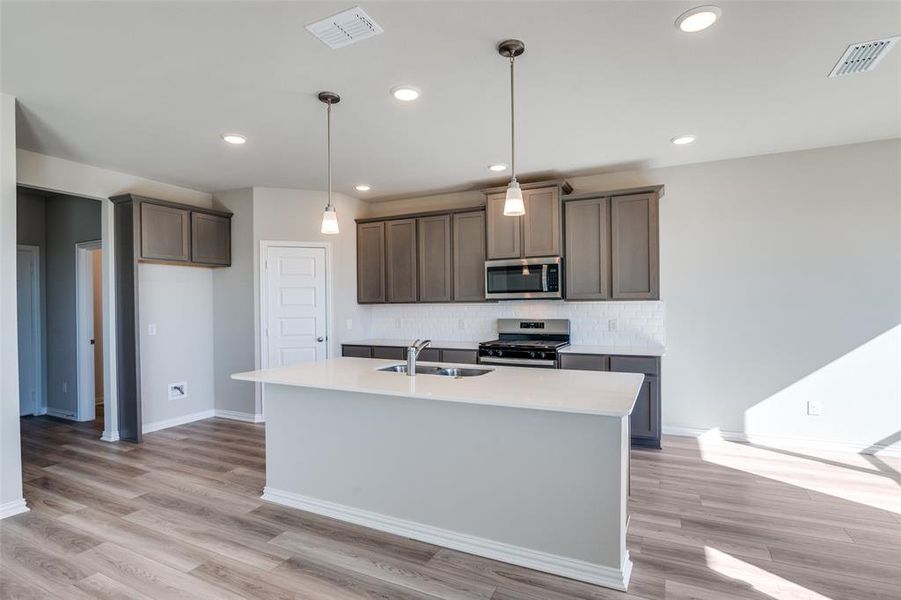 Kitchen with appliances with stainless steel finishes, decorative backsplash, decorative light fixtures, an island with sink, and recessed lighting Kitchen with appliances with stainless steel finishes, decorative backsplash, decorative light fixtures, an island with sink, and recessed lighting