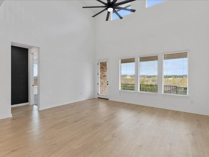 Unfurnished living room with healthy amount of natural light, light wood-style flooring, ceiling fan, and a towering ceiling