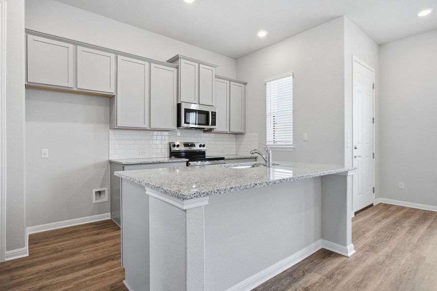Kitchen with light stone countertops, gray cabinetry, stainless steel appliances, decorative backsplash, and dark wood-style flooring