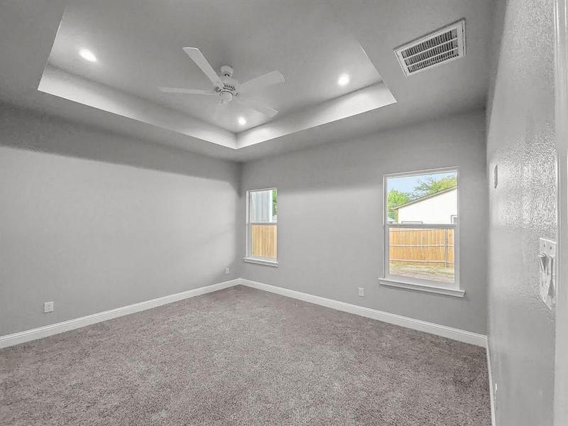 Primary bedroom featuring a tray ceiling, recessed lighting, ceiling fan, carpet flooring, and baseboards Primary bedroom featuring a tray ceiling, recessed lighting, ceiling fan, carpet flooring, and baseboards