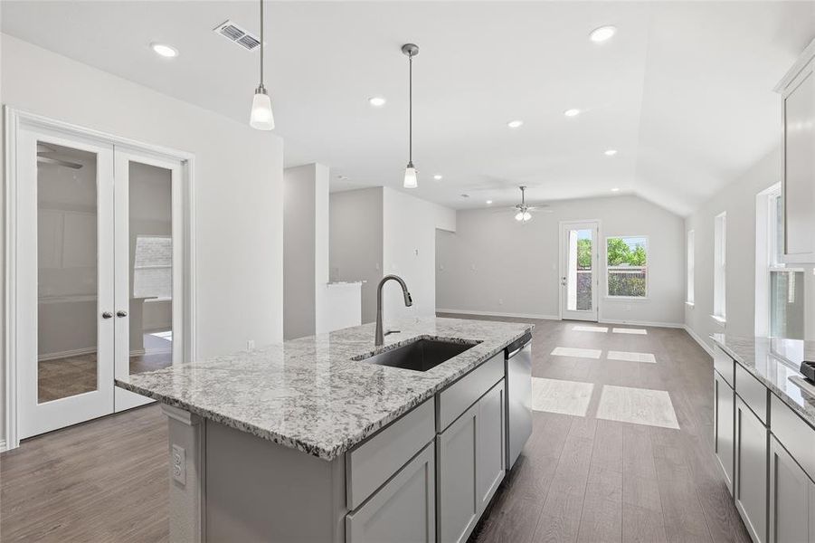 Kitchen featuring a ceiling fan, dark wood finished floors, an island with sink, light stone counters, and pendant lighting Kitchen featuring a ceiling fan, dark wood finished floors, an island with sink, light stone counters, and pendant lighting