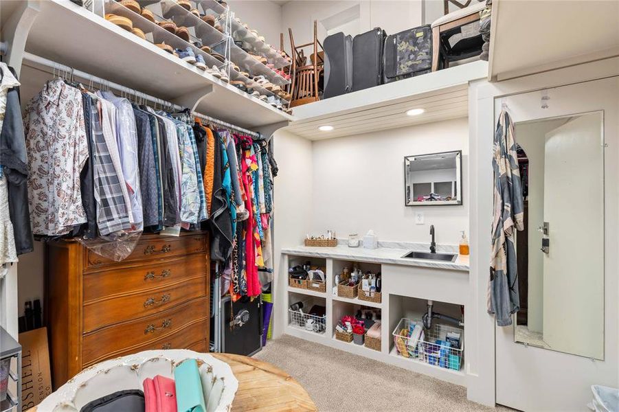 Custom closet organization system featuring extensive built-in shelving, hanging rods, recessed lighting, and a vanity area with a black sink, faucet, and framed mirror