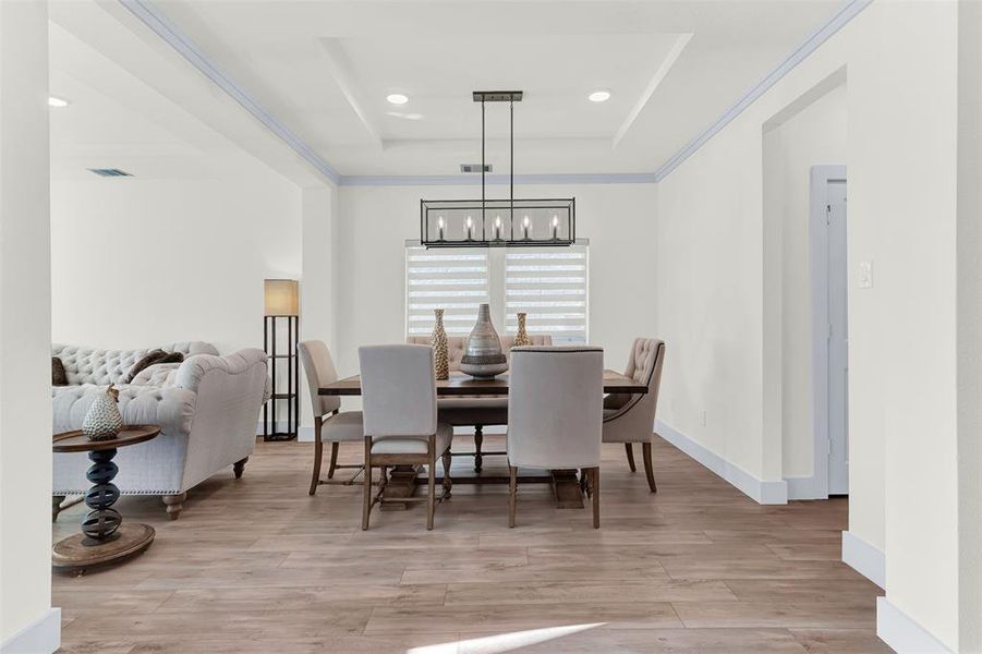 Dining area with a tray ceiling, light wood-style floors, a chandelier, and recessed lighting Dining area with a tray ceiling, light wood-style floors, a chandelier, and recessed lighting